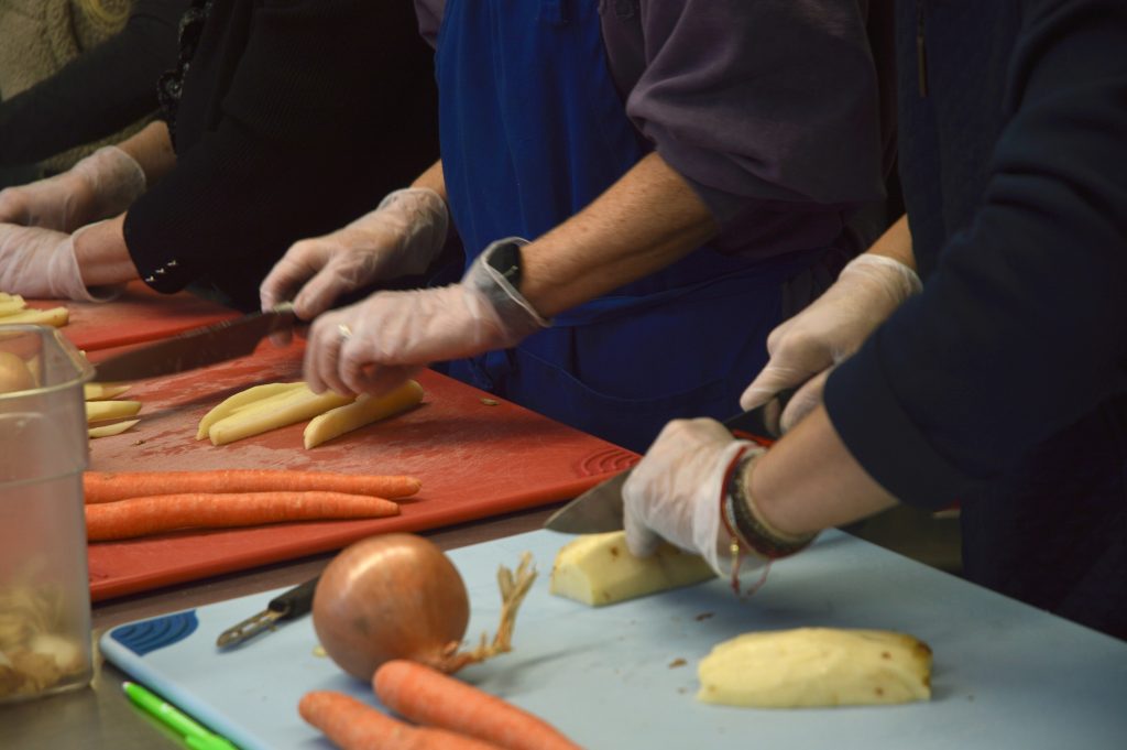 Three people cutting potato wedges with pairing knives while wearing gloves