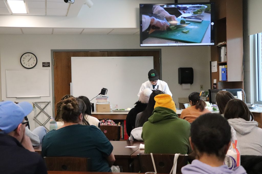 Individuals observe cooking demo at the front of the room