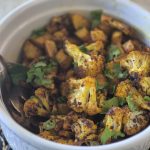 Mixture of seasoned cauliflower, potatoes, and garnish in a white bowl