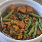 A Mixture of green beans, carrots, peas in a brown paste within a white bowl.