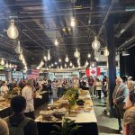 Table of dishes prepared in a large room with people listening to a chef speak.