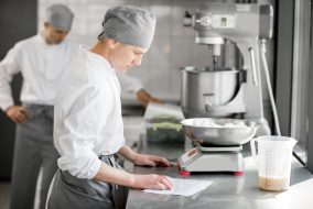 Two handsome male confectioners in uniform weighing ingredients for baking at the manufacturing