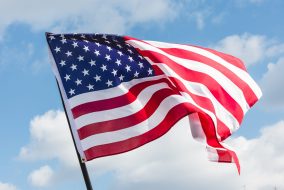 low angle view of stars and stripes on american flag against blue sky
