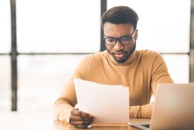 Reading Financial Reports. Concentrated black businessman reading papers at modern office, copyspace