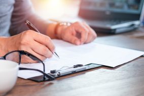 Close-up of Hand using writing pen with questionnaire or paperwork survey question filling in business company personal information form checklist document.