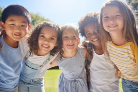 Happy, smile and portrait of kids in a park playing together outdoor in nature with friendship. Happiness, diversity and children friends standing, embracing and bonding in a outside green garden