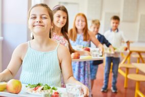 Smiling female students standing in line holding food trays during lunch time in school cafeteria