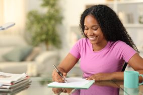 Happy black woman filling form sitting at home