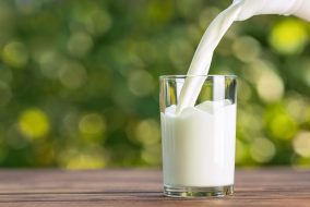 milk from jug pouring into glass on wooden table outdoors