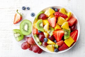 Bowl of healthy fresh fruit salad on wooden background. Top view.